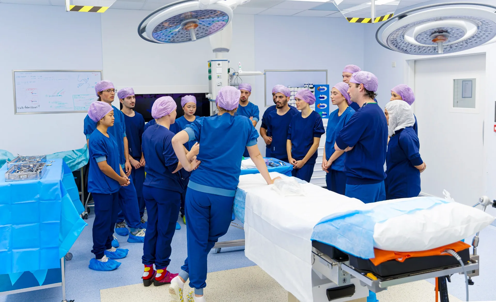 Cursisten en begeleiders staan samen rond de operatietafel tijdens een praktijkles.